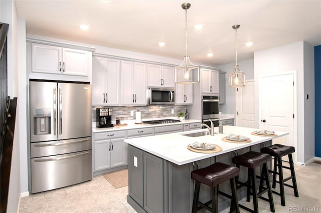 kitchen featuring a center island with sink, gray cabinets, stainless steel appliances, pendant lighting, and sink