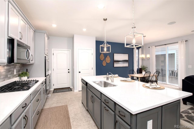 kitchen featuring gray cabinets, an island with sink, appliances with stainless steel finishes, hanging light fixtures, and sink