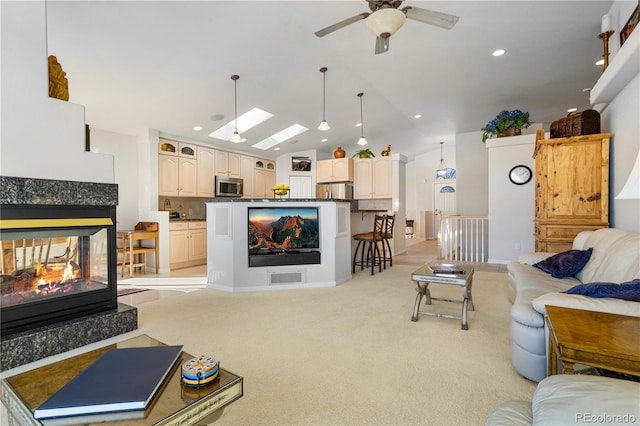 living room with light colored carpet, a fireplace, lofted ceiling with skylight, and ceiling fan