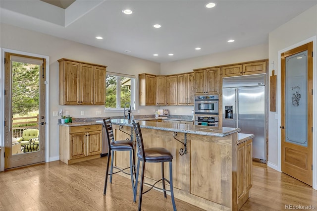 kitchen with light stone countertops, a center island, light hardwood / wood-style floors, and appliances with stainless steel finishes