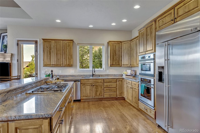 kitchen with light stone counters, stainless steel appliances, light hardwood / wood-style floors, and sink