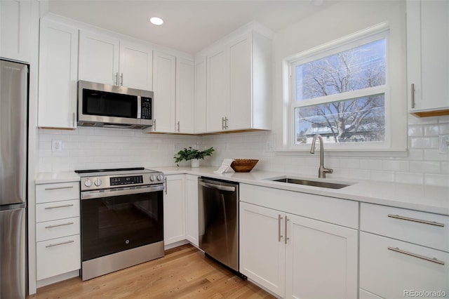 kitchen with a sink, white cabinetry, appliances with stainless steel finishes, light wood-type flooring, and decorative backsplash