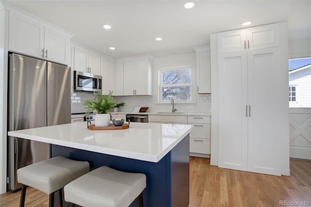 kitchen featuring appliances with stainless steel finishes, light wood-style floors, white cabinetry, a sink, and a kitchen breakfast bar