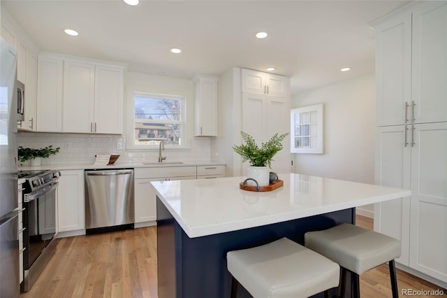 kitchen featuring range with electric stovetop, stainless steel dishwasher, light wood-style floors, a sink, and a kitchen breakfast bar