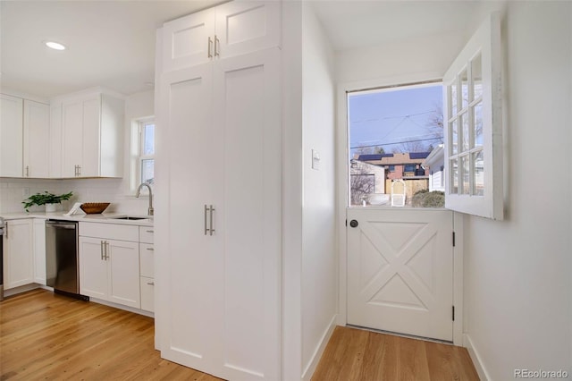 kitchen with light wood-type flooring, white cabinets, dishwasher, and a sink