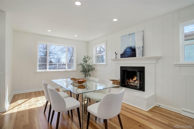 dining space with a brick fireplace, baseboard heating, a decorative wall, and wood finished floors