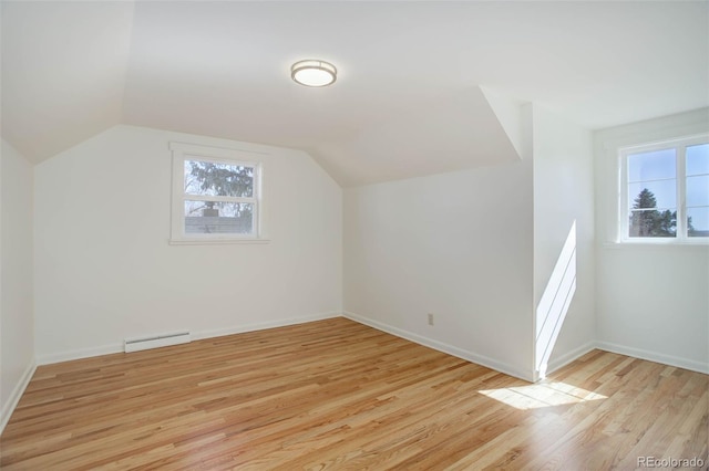 additional living space featuring vaulted ceiling, light wood finished floors, baseboard heating, and baseboards