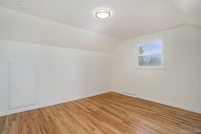 additional living space featuring a baseboard heating unit, light wood finished floors, lofted ceiling, and baseboards