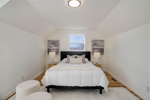 bedroom with lofted ceiling, visible vents, baseboards, and wood finished floors