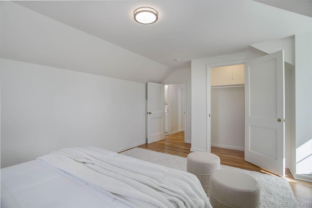 bedroom featuring lofted ceiling, a closet, light wood-style flooring, and baseboards