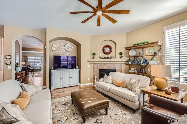 living room featuring a tiled fireplace, ceiling fan, a textured ceiling, and light hardwood / wood-style flooring