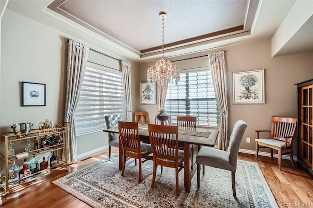 dining space with wood-type flooring, a chandelier, and a tray ceiling