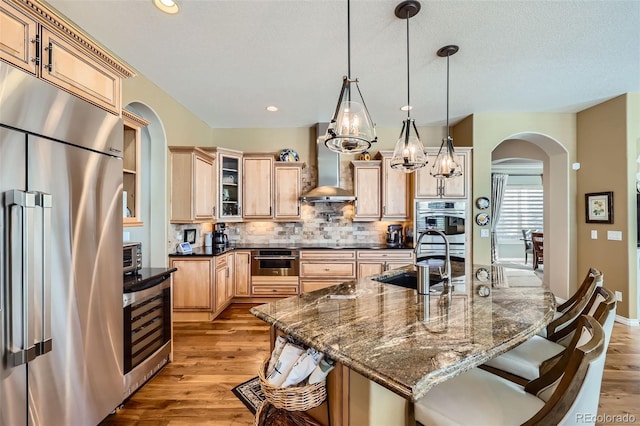 kitchen featuring sink, a breakfast bar, appliances with stainless steel finishes, beverage cooler, and wall chimney exhaust hood