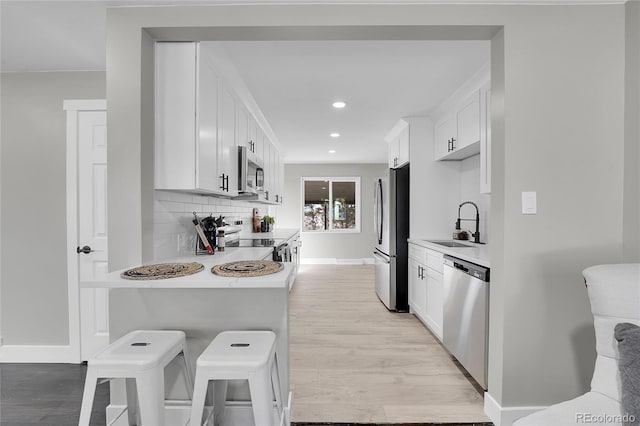 kitchen featuring stainless steel appliances, a sink, light wood-style floors, light countertops, and backsplash