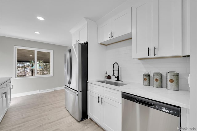 kitchen featuring light stone counters, light wood-style flooring, stainless steel appliances, a sink, and white cabinetry