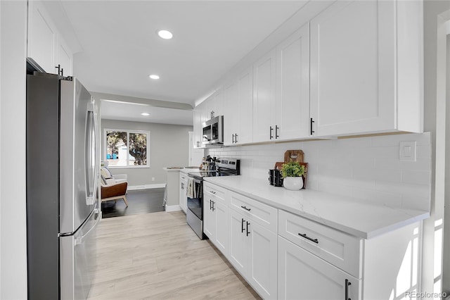 kitchen featuring light stone counters, white cabinetry, light wood-style floors, appliances with stainless steel finishes, and decorative backsplash