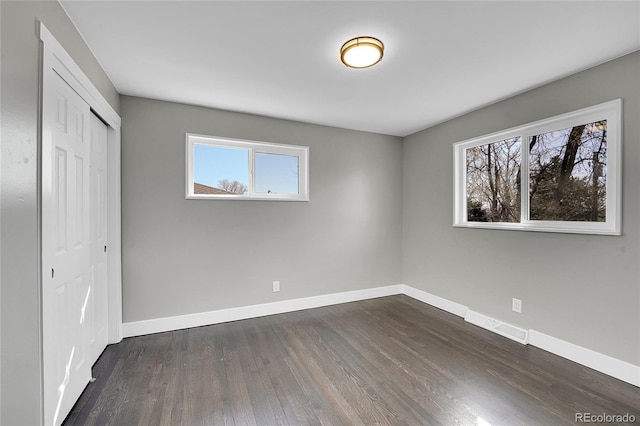 unfurnished bedroom featuring a closet, dark wood-style flooring, visible vents, and baseboards