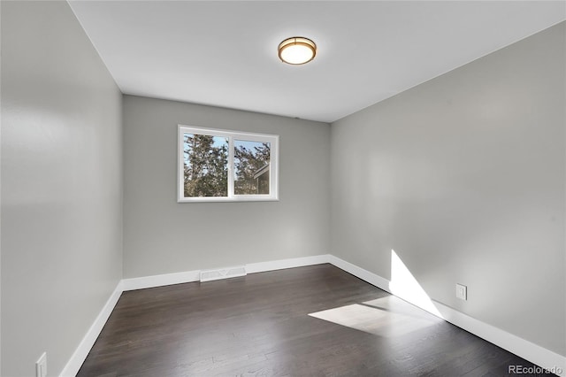 empty room with dark wood-style floors, visible vents, and baseboards