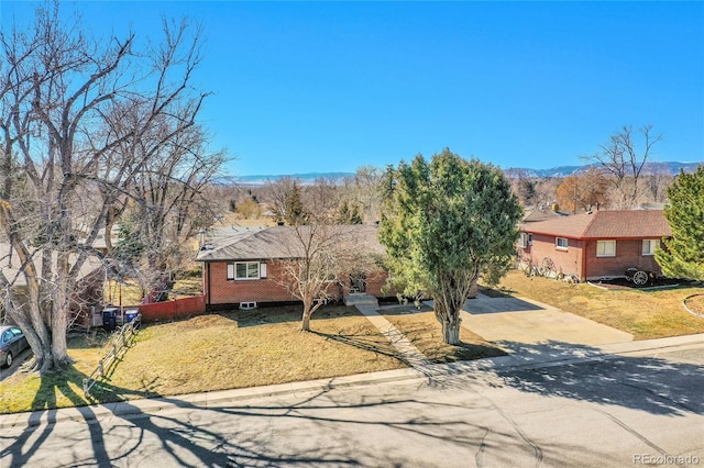 view of front of house with concrete driveway, brick siding, a mountain view, and a front lawn