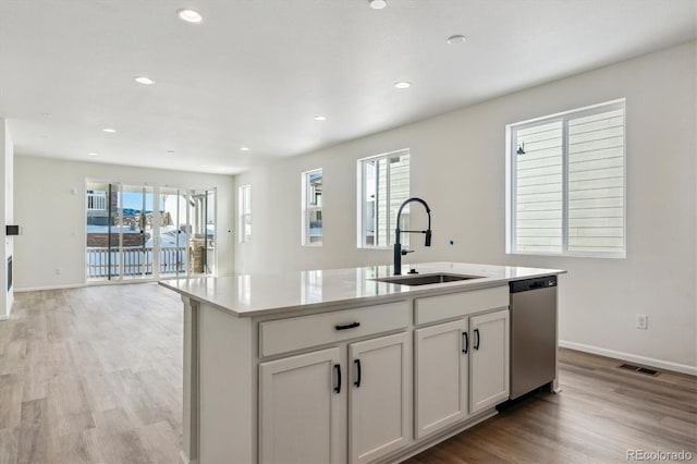 kitchen with light wood-type flooring, a kitchen island with sink, sink, dishwasher, and white cabinetry