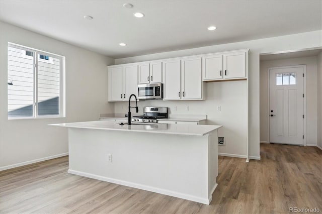 kitchen with appliances with stainless steel finishes, a center island with sink, and white cabinetry