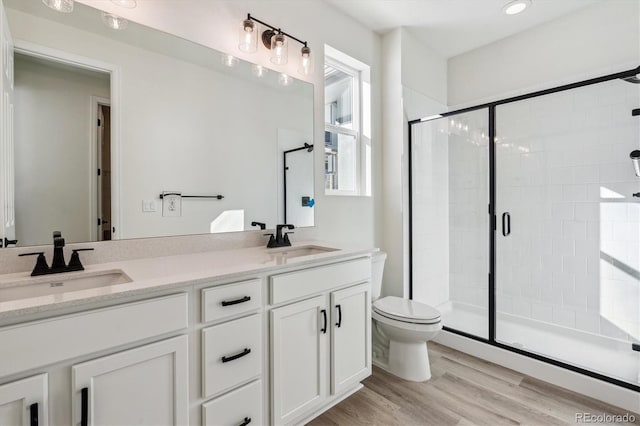 bathroom featuring hardwood / wood-style floors, vanity, a shower with shower door, and toilet