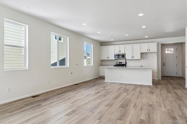 kitchen with white cabinets, light wood-type flooring, an island with sink, and appliances with stainless steel finishes