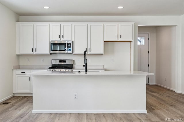 kitchen featuring a kitchen island with sink, white cabinets, light hardwood / wood-style floors, and appliances with stainless steel finishes