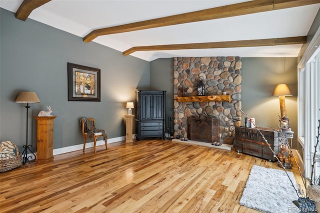 living area featuring baseboards, a stone fireplace, lofted ceiling with beams, and wood finished floors