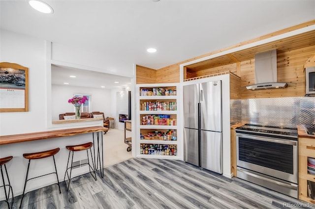 935 Newark St, Aurora, CO 80010 - kitchen featuring appliances with stainless steel finishes, wall chimney exhaust hood, light wood-style flooring, decorative backsplash, and recessed lighting