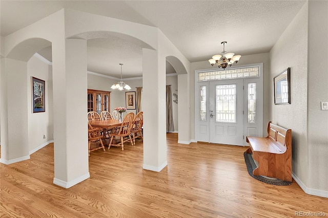 19045 Shiloh Ranch Dr, Colorado Springs, CO 80908 - foyer entrance with a chandelier, arched walkways, light wood finished floors, a textured ceiling, and crown molding