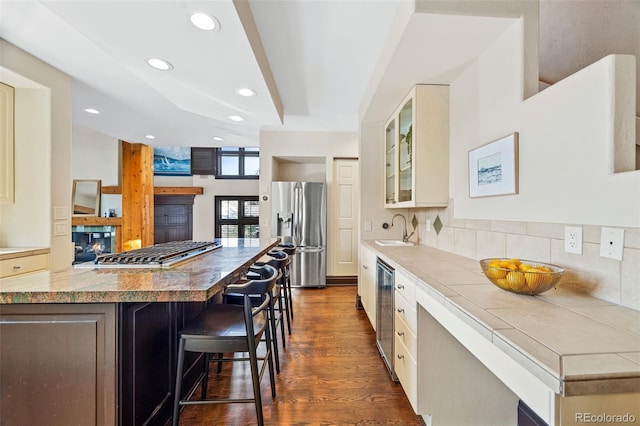 kitchen with decorative backsplash, glass insert cabinets, a kitchen bar, stainless steel refrigerator with ice dispenser, and a sink