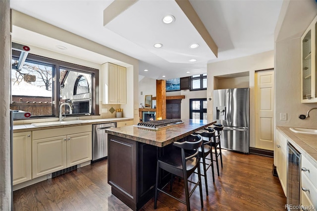 kitchen with a sink, light countertops, appliances with stainless steel finishes, a center island, and glass insert cabinets