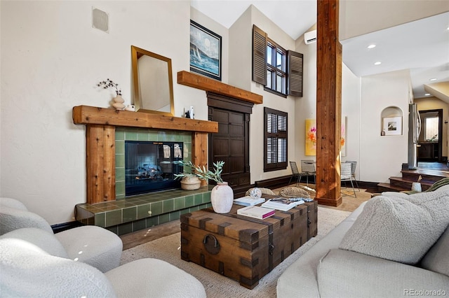 living room with visible vents, an AC wall unit, a healthy amount of sunlight, high vaulted ceiling, and a tile fireplace