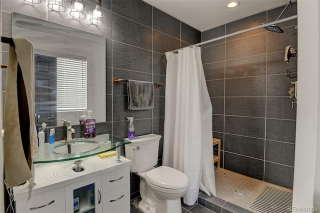 bathroom with tile walls, a tile shower, toilet, vanity, and recessed lighting