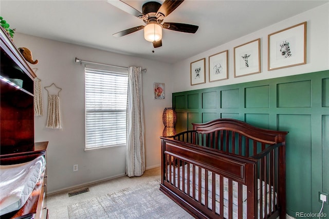 carpeted bedroom featuring a nursery area and ceiling fan