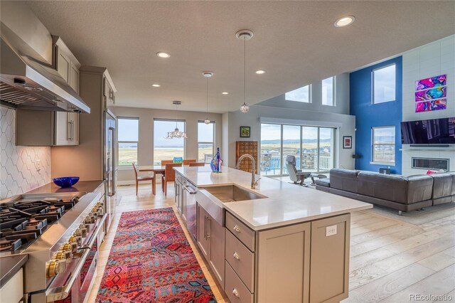 kitchen featuring double oven range, a center island with sink, sink, decorative backsplash, and decorative light fixtures