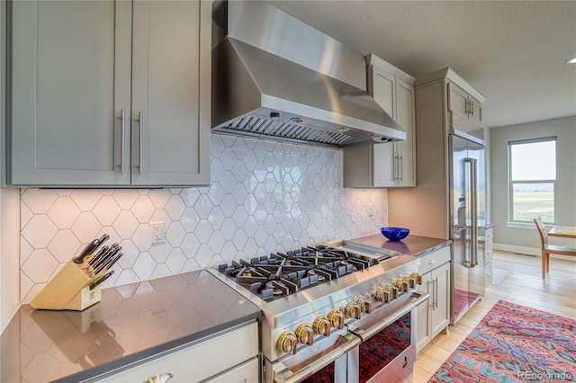 kitchen featuring premium appliances, tasteful backsplash, gray cabinets, and wall chimney range hood