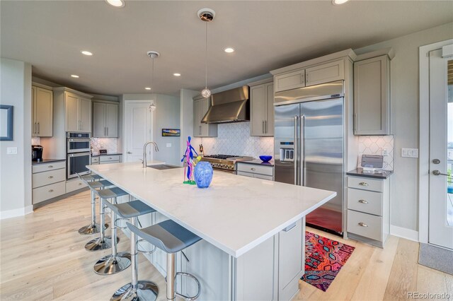 kitchen with sink, wall chimney exhaust hood, gray cabinets, appliances with stainless steel finishes, and decorative light fixtures