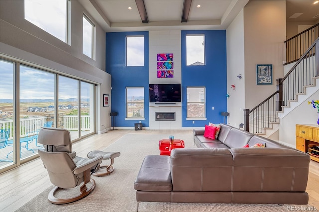 living room with beamed ceiling, a high ceiling, and light hardwood / wood-style floors