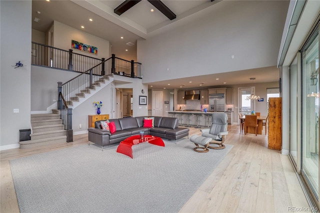 living room featuring beam ceiling, a towering ceiling, light hardwood / wood-style floors, and an inviting chandelier