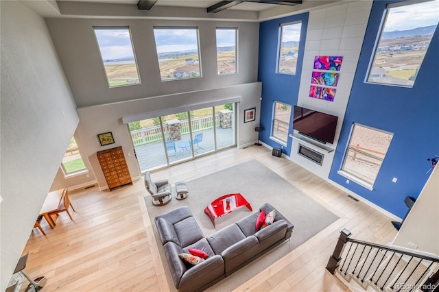 living room with beam ceiling, light wood-type flooring, and a high ceiling