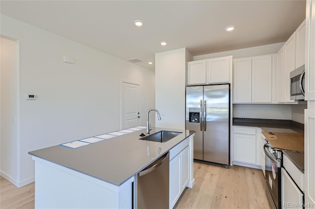 kitchen featuring stainless steel appliances, a sink, white cabinets, light wood-type flooring, and dark countertops