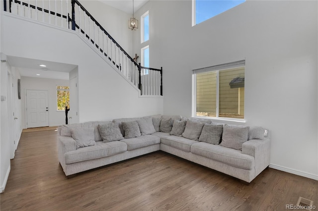 living room with an inviting chandelier, a towering ceiling, a wealth of natural light, and dark hardwood / wood-style flooring