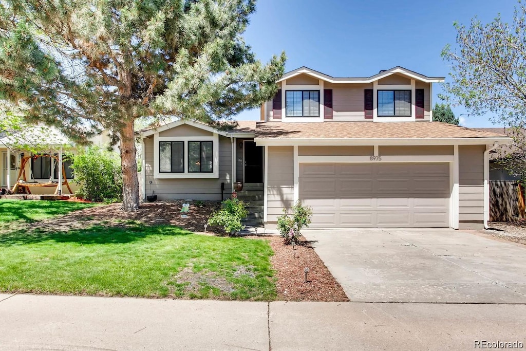 tri-level home with a front lawn, driveway, a shingled roof, and a garage