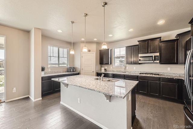 785 Iris St, Brighton, CO 80601 - kitchen with appliances with stainless steel finishes, a kitchen bar, a center island with sink, light stone counters, and dark wood-type flooring