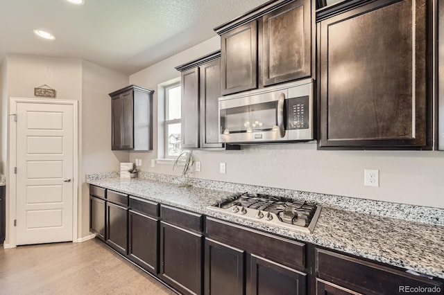785 Iris St, Brighton, CO 80601 - kitchen with appliances with stainless steel finishes, light wood finished floors, dark brown cabinets, light stone counters, and recessed lighting
