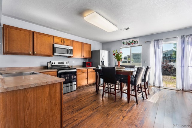 4528 Andes St, Denver, CO 80249 - kitchen featuring stainless steel appliances, brown cabinets, dark wood-style flooring, a textured ceiling, and a sink
