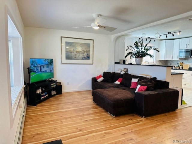 living area featuring a ceiling fan, light wood-type flooring, and baseboards