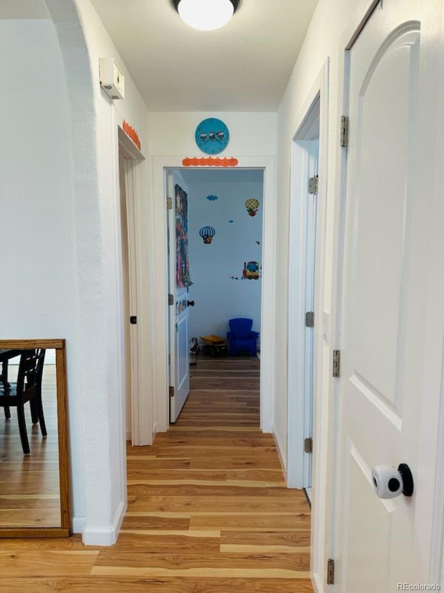 hall featuring arched walkways, light wood-style flooring, and baseboards